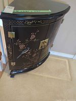 Front and side view showing overall cabinet shape, painted design, brass hardware, glass top
