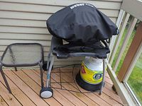 Weber grill with cover, propane tank on stand, glass side table
