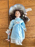 Full view of porcelain doll lying flat showing dress, hat, parasol, shoes