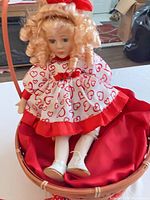 Full view of doll seated in wicker basket showing dress, hair and basket handle
