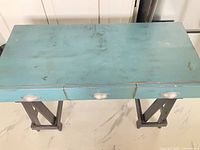 Top view of turquoise/teal console table with drawers closed and X-frame legs visible