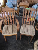Front view of both wooden dining chairs showing backs, arms, and seat upholstery
