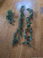 Three artificial hanging garland vines laid out on wood floor showing styles and lengths