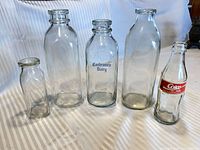 Front view of five clear glass bottles including three milk bottles, one Cochrane’s Dairy milk bottle, and one Coca-Cola contour soda bottle