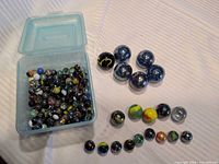 Open Sterilite box filled with assorted marbles; additional shooters and selected marbles displayed beside