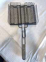 Full view of steel wire grilling basket showing wooden handle and hinged grid