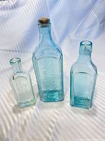 Front view of all three aqua glass bottles showing embossing and relative sizes