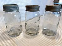 Front view of three embossed glass jars showing brands and lids