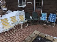 Five of the folding chairs lined up outdoors showing yellow/white strap, green sling and blue webbing examples
