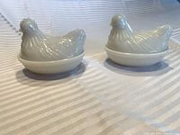 Pair of white milk glass hen-on-nest covered dishes with lids on bases