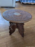 Full view of round hand-carved wooden accent table on floor