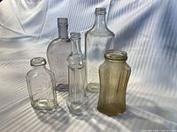 Front view of all five clear glass bottles showing shapes and condition
