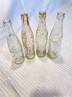 Front view of four empty glass soda bottles showing brand embossing and condition