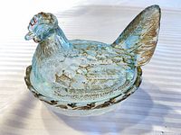 Side view of glass hen on nest showing gilt details and rim