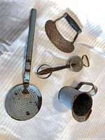 All four vintage metal kitchen tools laid out: skimmer, egg beater, mezzaluna, pitcher
