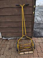 Full view of yellow push reel lawn mower leaning against wall