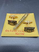 Set of cufflinks and tie clip on gold fabric card showing damascene design