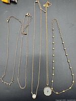 Five gold-tone necklaces laid out for overview
