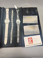 Open presentation case displaying two watches, bracelet, warranty cards