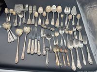Overview of entire assortment of mixed silver-plated flatware laid out on black background