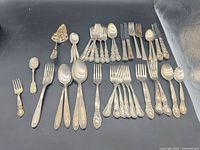 Full lot overview showing all mixed silverplate flatware pieces laid out