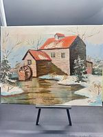 Front view of signed winter watermill painting on easel
