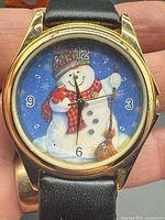 Front view of wristwatch showing snowman dial and gold-tone case