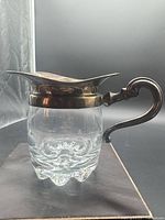 Profile view of creamer showing glass body, sterling collar and handle