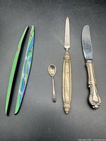 All four items laid out: enameled sticks, demitasse spoon, letter opener, butter knife