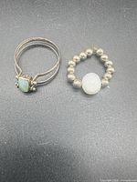 Two sterling silver rings on black background: split-shank with green stone, beaded stretch with white druzy