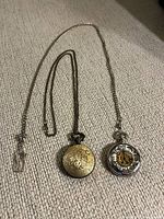 Both pocket watches closed showing exterior designs and chains