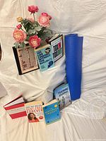 All six books, rolled blue yoga mat and artificial pink floral arrangement displayed together