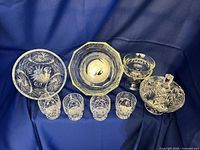 All eight crystal pieces—two bowls, four tumblers, compote, lidded dish—displayed on blue backdrop
