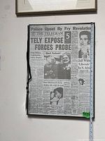 Black-framed newspaper front page artwork with tape measure for scale