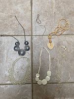 Six necklaces laid out: disc statement, herringbone, wood bead heart, faux-pearl collar, resin discs, faux-pearl strands