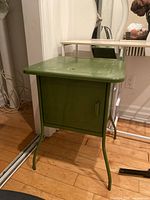 Front view of green metal side table showing cabinet door and legs