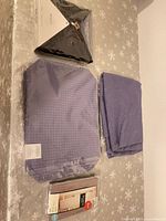 All four items laid out: black tablecloth, purple tablecloth, purple placemats, window sheer package