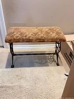 Full view of upholstered bench showing seat fabric and ornate iron legs