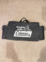 Black Cookin’ with Coleman vinyl carry case, side pockets and handle visible