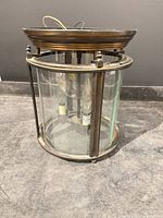Full view of cylindrical pendant showing glass panels, metal frame, canopy, wiring, bulb sockets