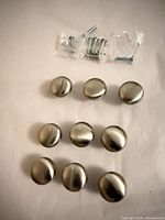 Front view of nine brushed nickel cabinet knobs with screws in bags