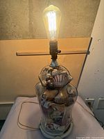 Lamp illuminated, showing glass body with seashells, wood base, bulb lit