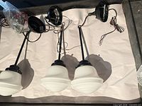 Three pendant lights with white shades and black hardware laid out on surface