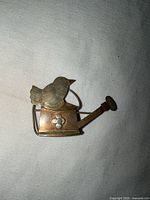 Front view of brooch showing bird, watering can shape, flower detail