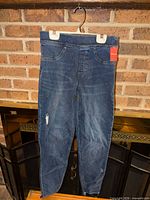 Front view of dark denim Spanx jeggings on hanger showing overall condition and style