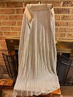 Full front view of metallic gold pleated maxi skirt hanging, displaying length and pleats