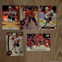 Group shot of five Cole Caufield Upper Deck hockey cards laid out on wood surface, showing fronts of all cards