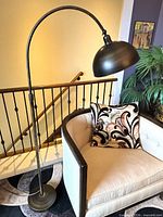 Full view of brushed bronze arc floor lamp beside chair