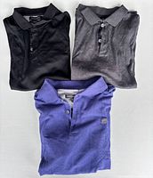 Three folded polo shirts in black, charcoal and royal blue