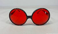 Front view of sunglasses showing round red lenses and black frame